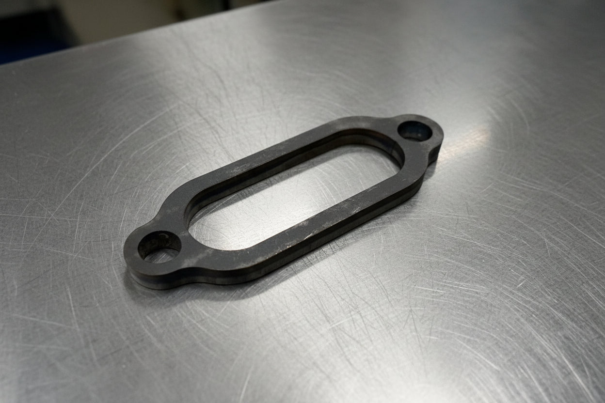 A black steel exhaust flange laid on a grey surface.